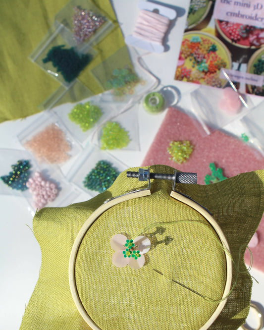 Embroidery hoop with green fabric and floral design, surrounded by embroidery supplies on a table.