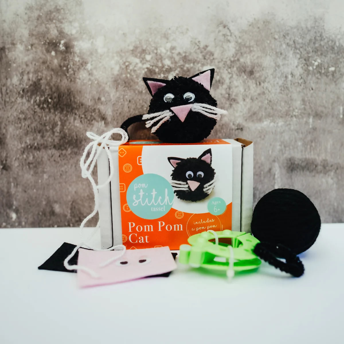 Black pom-pom cat toy with packaging on a textured surface
