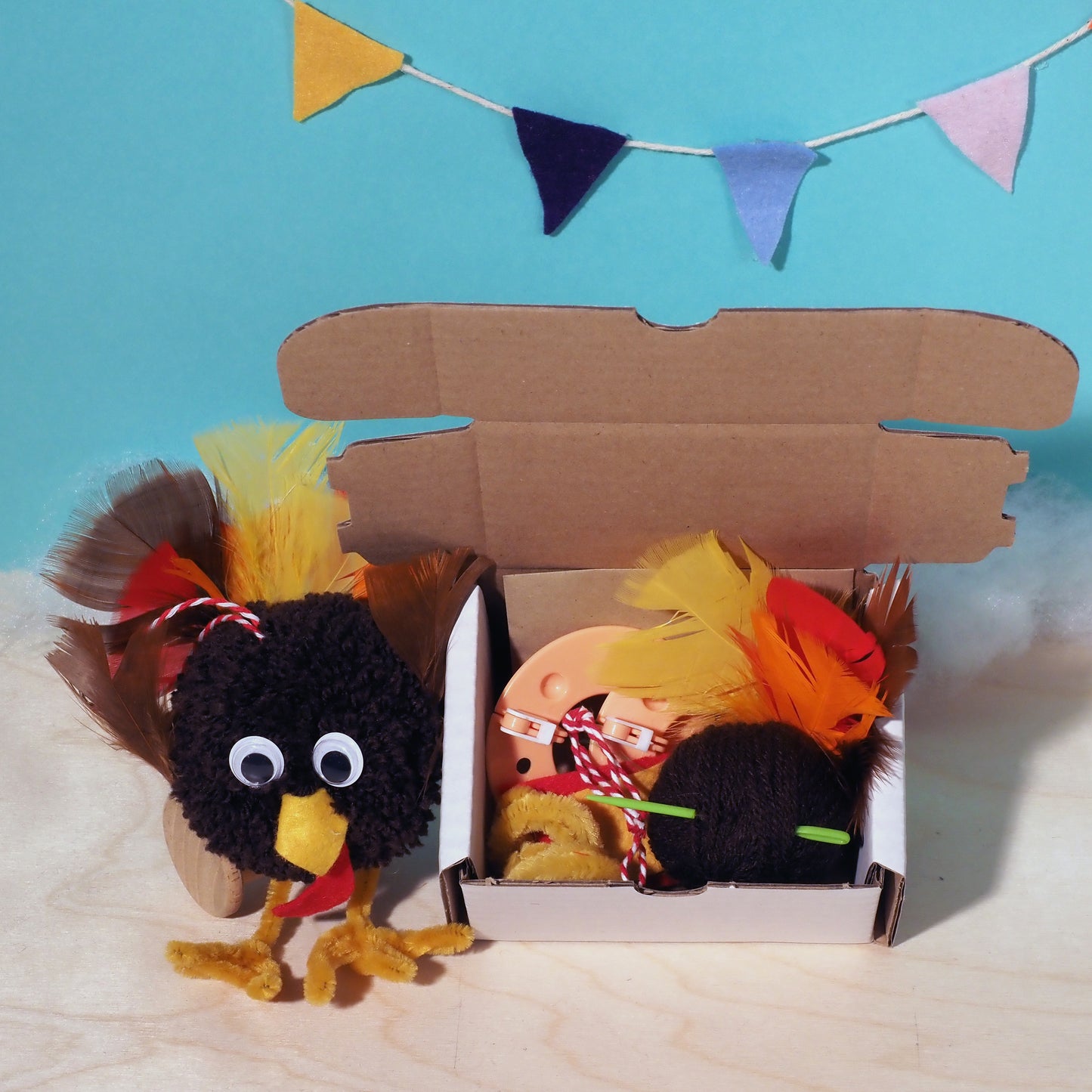 Toy birds with colorful feathers in a cardboard box against a blue background with colorful flags.