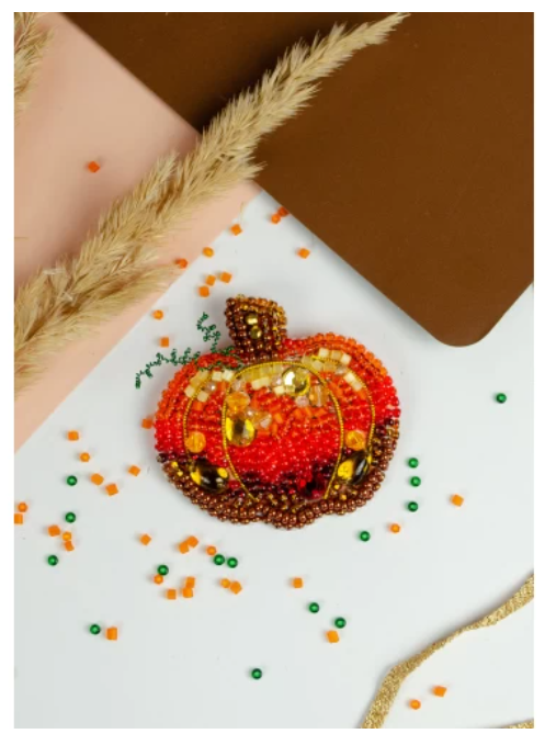 Decorative brooch shaped like a pumpkin with beads on a white background.