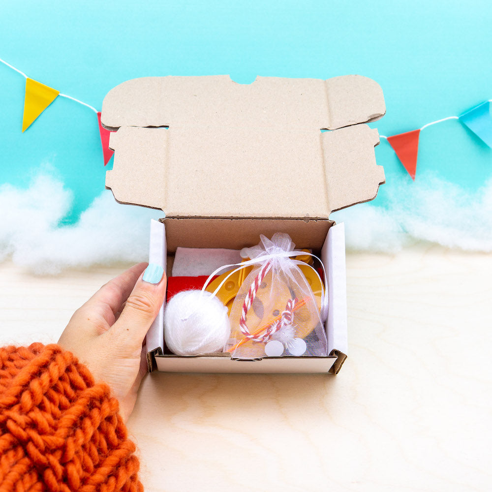Hand holding a box with festive items against a light blue background with colorful flags.