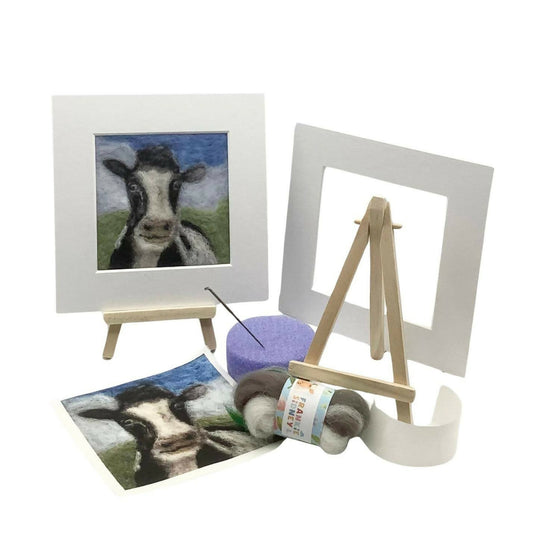 Artistic materials including a framed picture of a cow, a yarn ball, and a small easel on a white background.