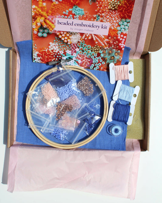 Beaded embroidery kit with hoop, beads, and tools in an open box on a white background