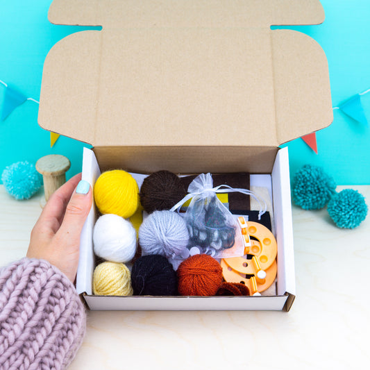 Open box containing yarn balls and knitting tools on a blue background