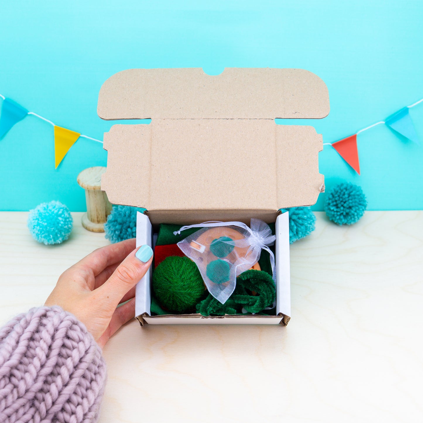 Hand opening a cardboard box with decorative items on a light blue background