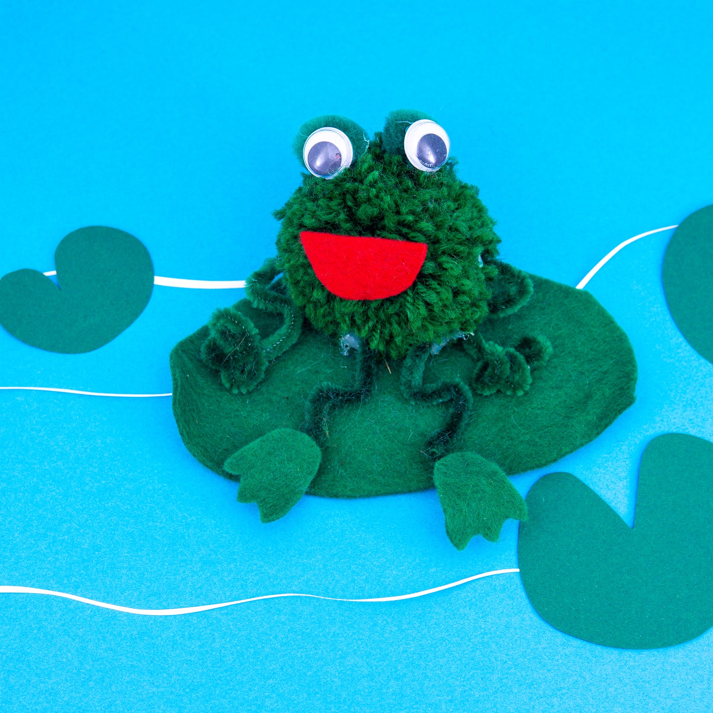 Green frog plush toy on a blue background with leaf decorations