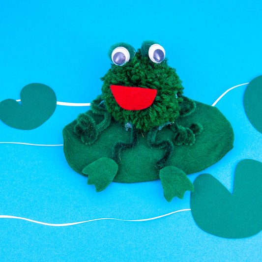 Green frog plush toy on a blue background with leaf decorations
