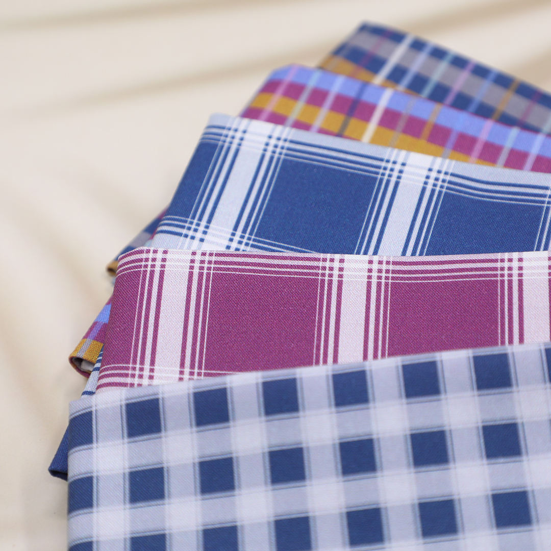 Stack of plaid fabric samples in various patterns on a beige background