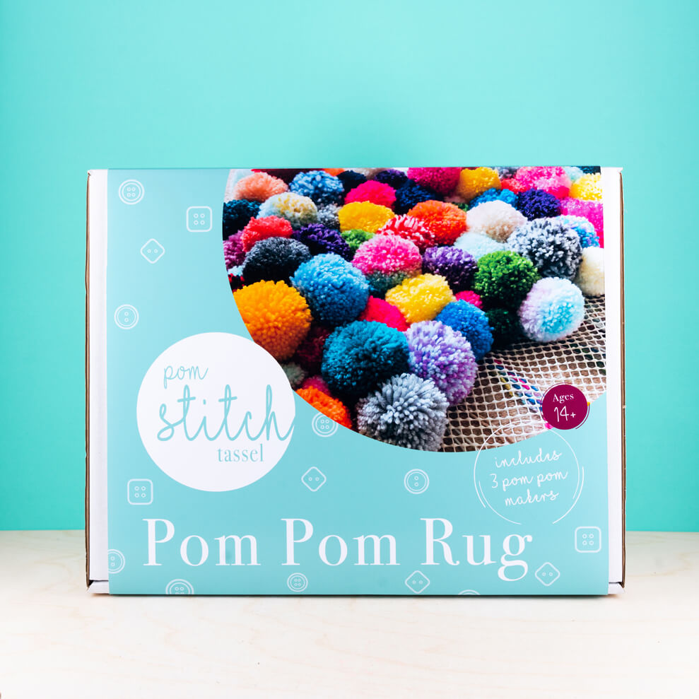 Box for making a pom pom rug with colorful pom poms on a blue background
