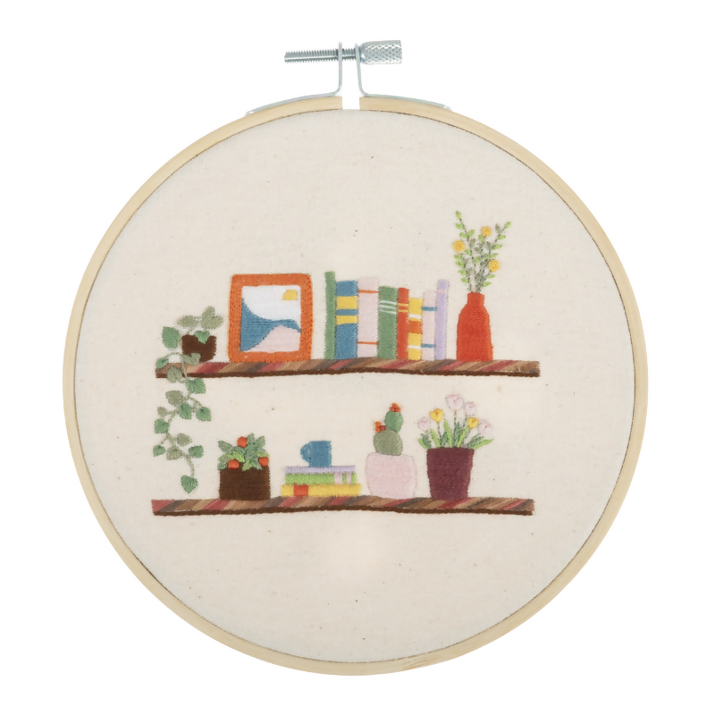Embroidery hoop with a colorful depiction of books and plants on shelves.