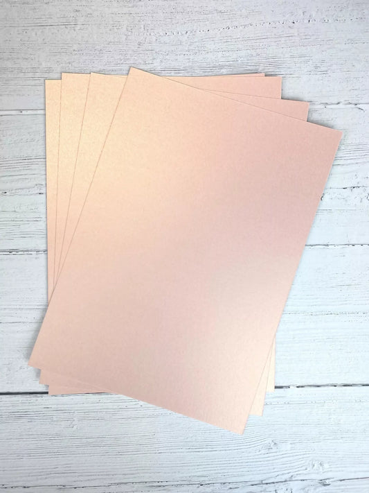 Three sheets of beige pearl card on a light wooden surface