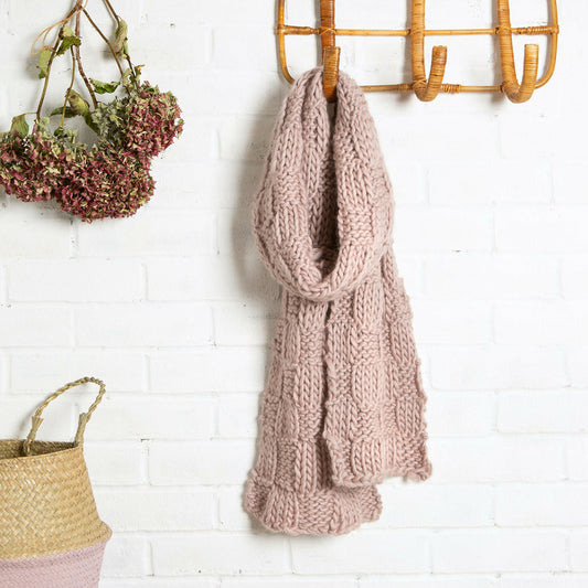 Knitted scarf hanging on a wooden hook against a white brick wall.