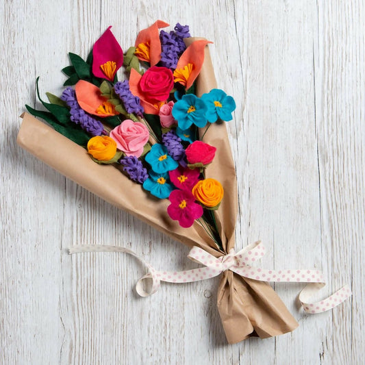 Colorful bouquet of flowers wrapped in brown paper with a pink ribbon on a light wooden surface.