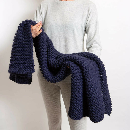 Person holding a navy blue knitted blanket against a plain background