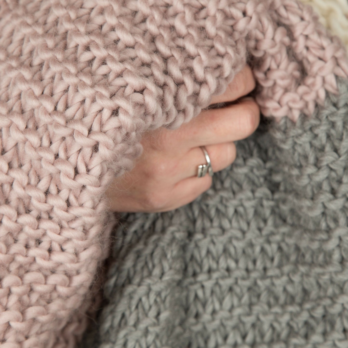 Close-up of a hand holding a pink knitted blanket with a gray blanket underneath.