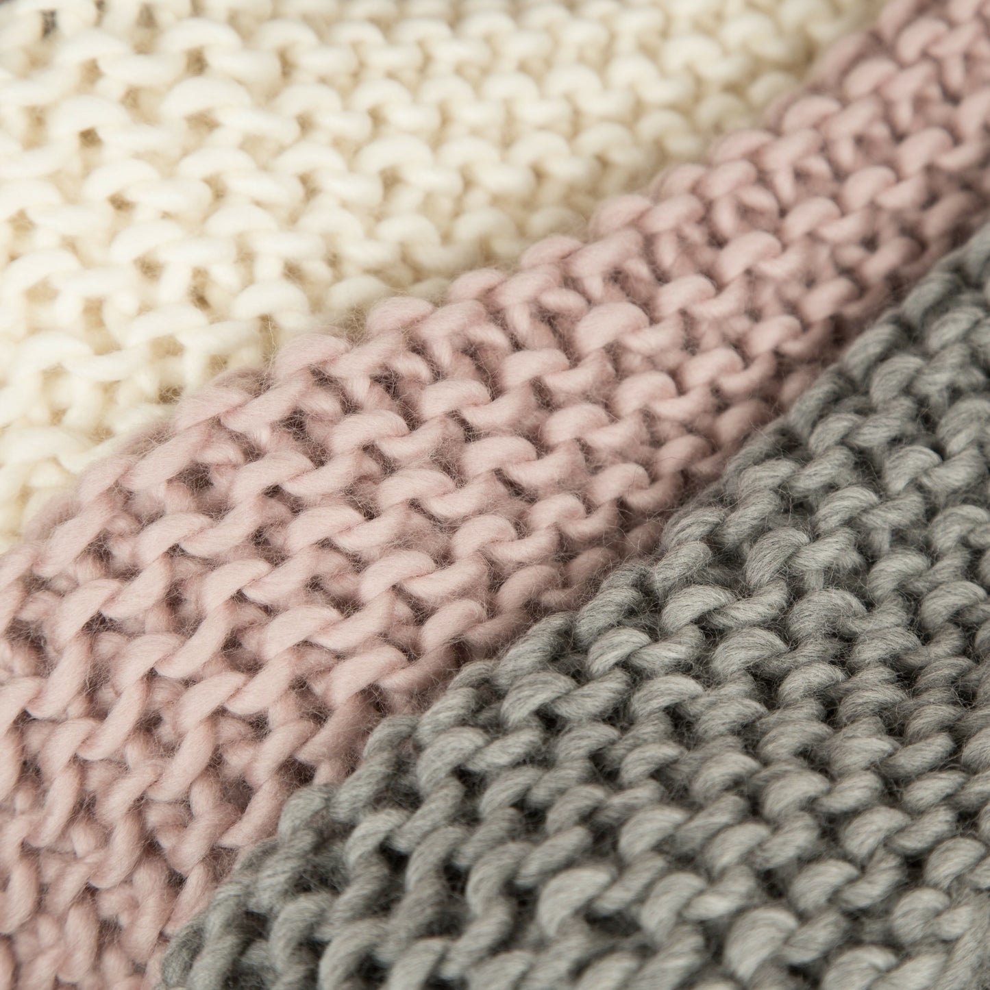 Close-up of three knitted fabrics in beige, pink, and gray.