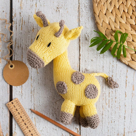 Knitted giraffe toy on a wooden surface with a ruler and leaf decoration.