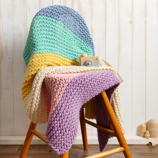 A finished, chunky knit blanket in pastel colors, made with a Wool Couture kit.