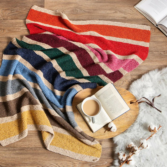 Colorful striped blanket draped over a wooden surface with a cup of coffee and book.