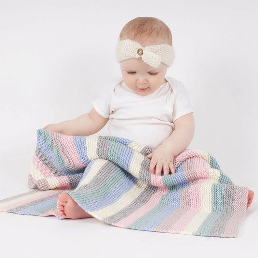Baby sitting on a colorful striped blanket wearing a white headband.