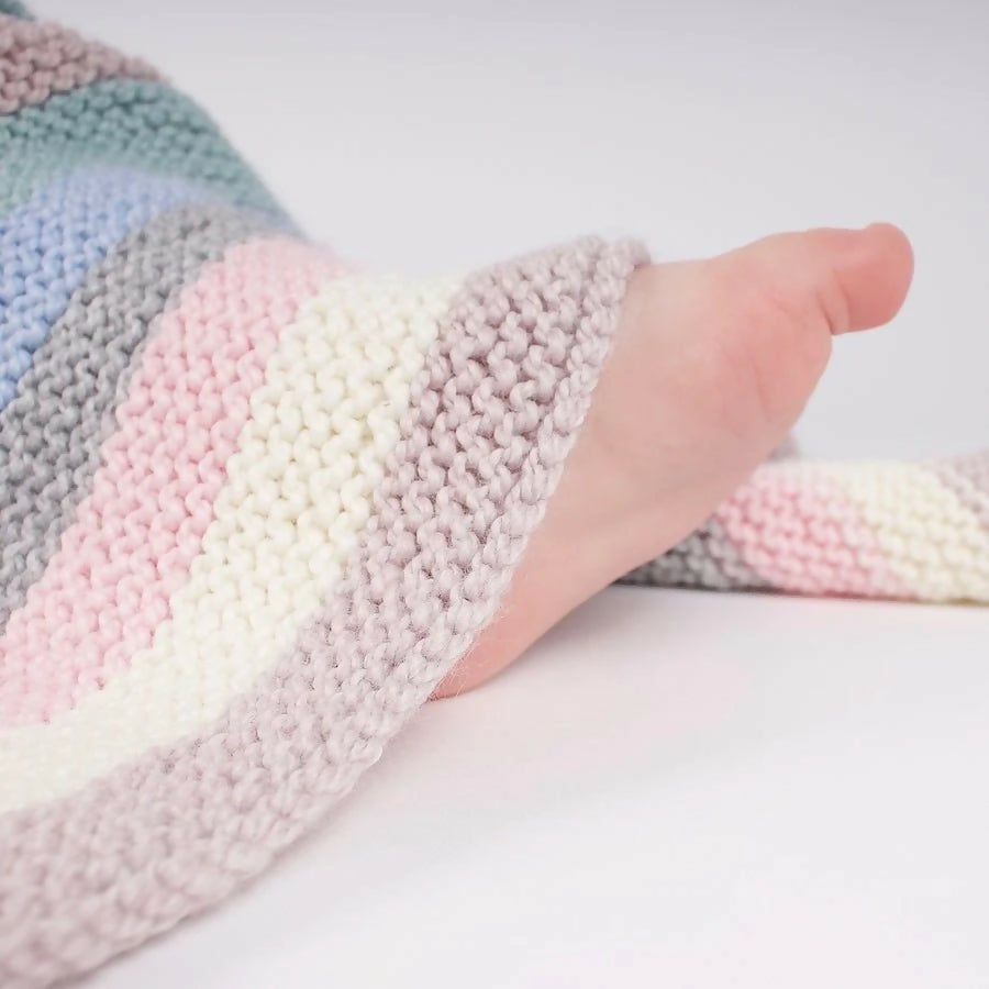 Pastel striped knitted blanket with a hand peeking out from under it on a white background