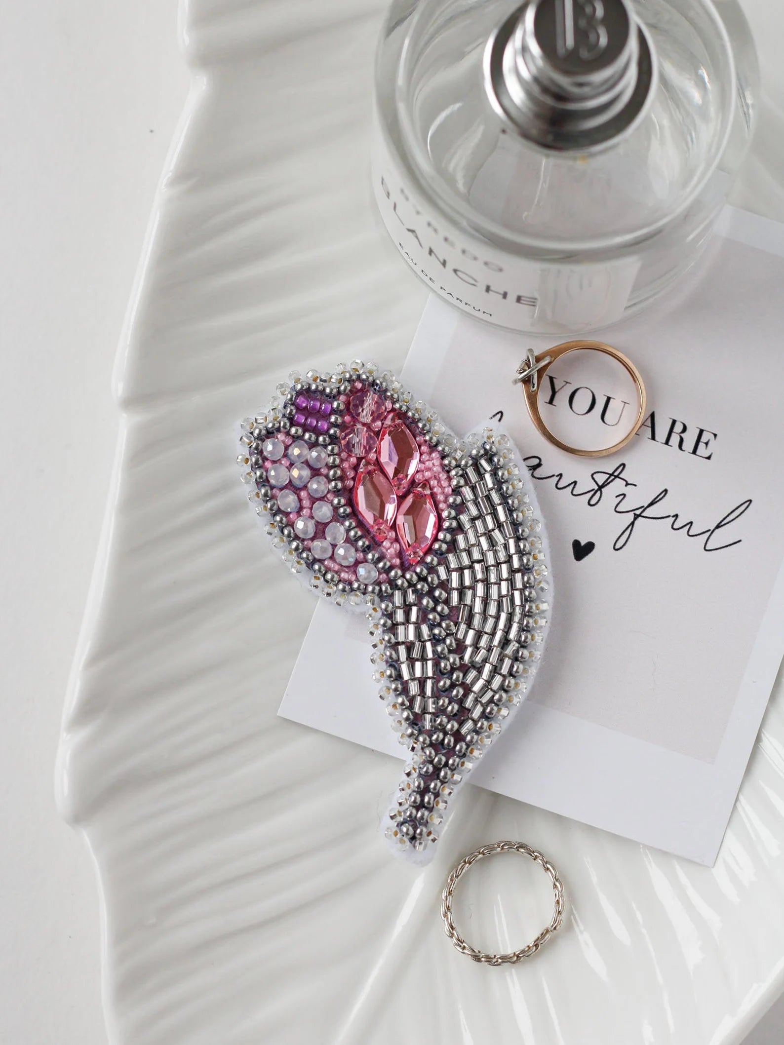 Decorative brooch with pink gemstones on a white surface with a perfume bottle and card.