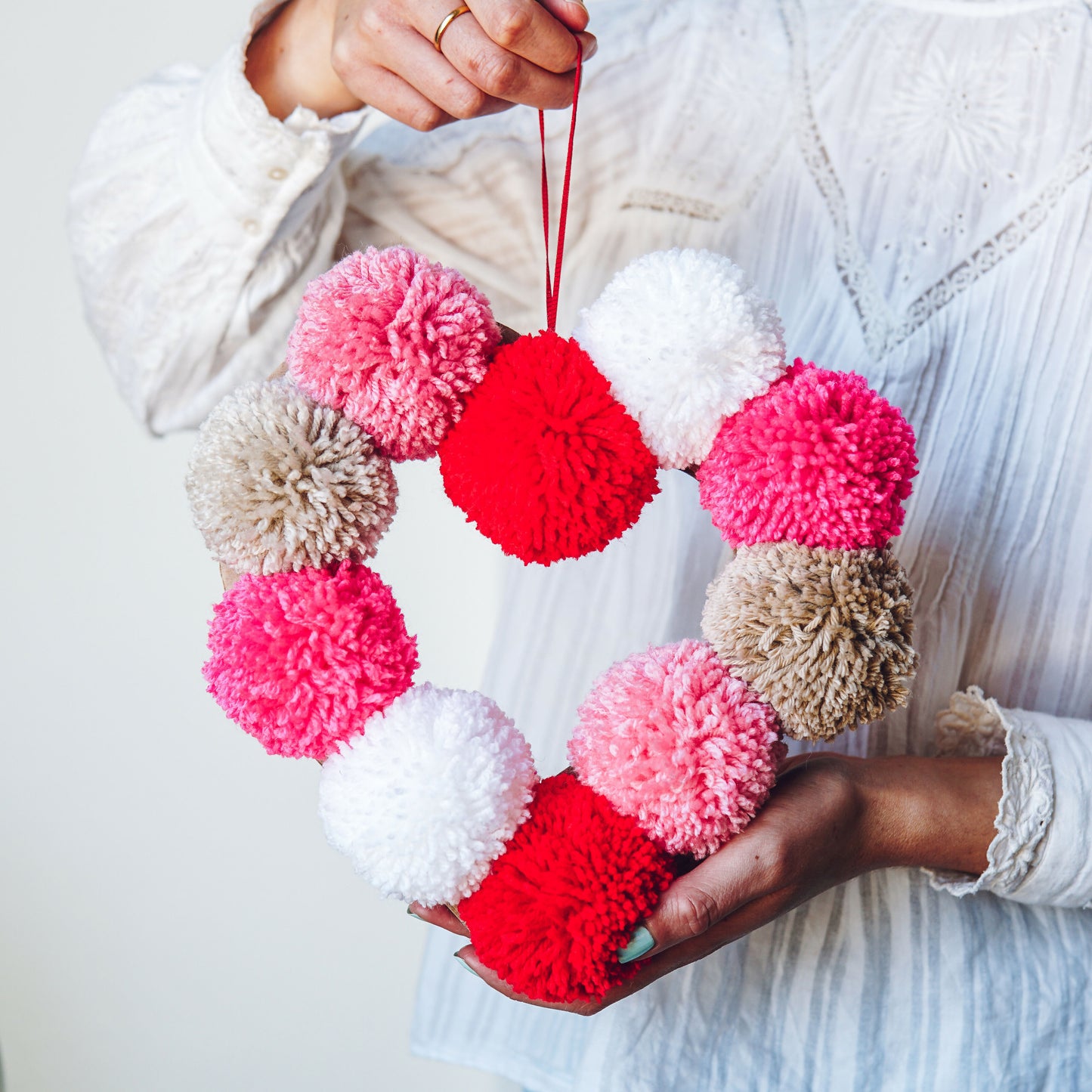 Heart-shaped wreath made of colorful pom-poms held by a person against a light background
