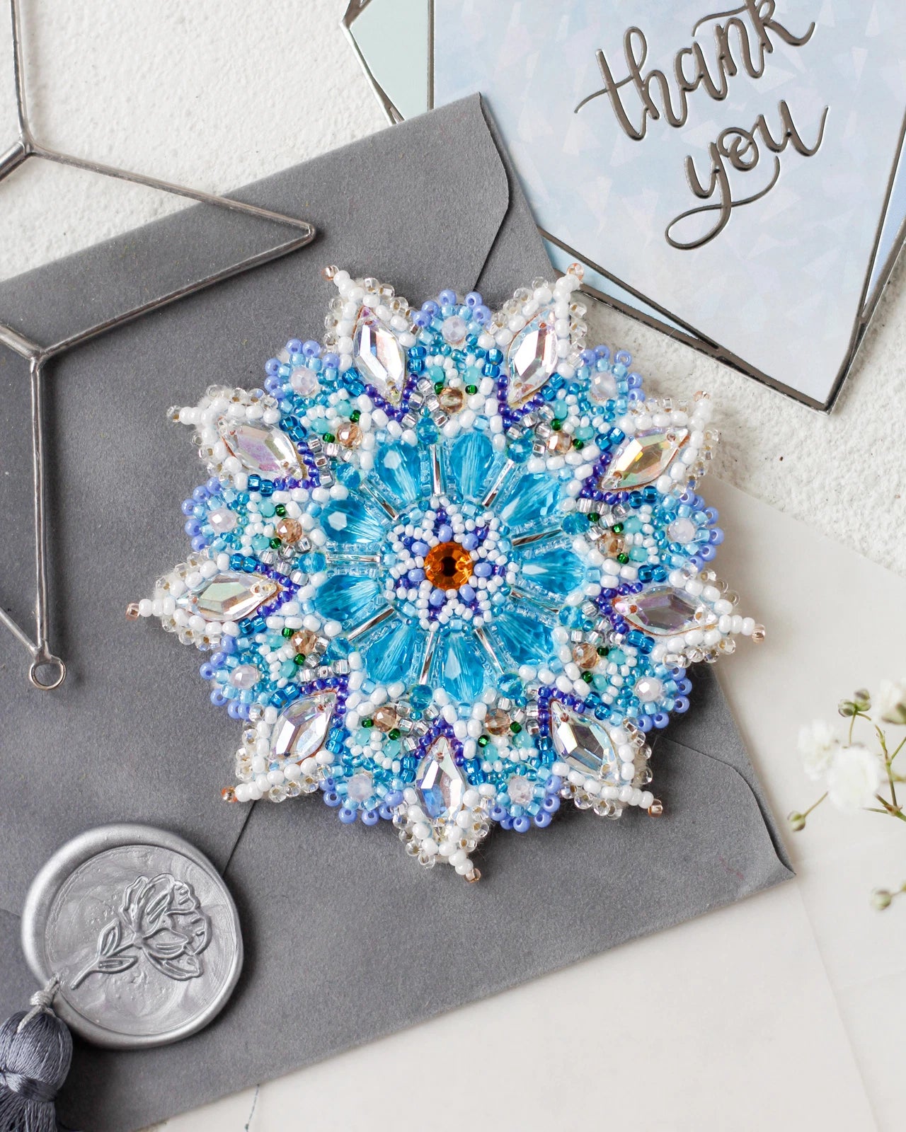 Decorative brooch with blue gemstones on a gray surface with 'thank you' card in the background