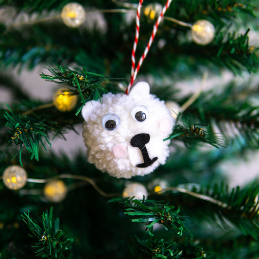 White pom-pom ornament shaped like a bear on a Christmas tree with lights.