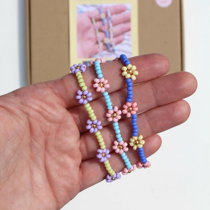Hand holding three colorful beaded flower necklaces with a blurred background