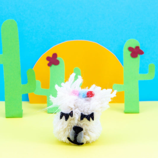 Toy llama with colorful accents on a blue and yellow background with cacti.