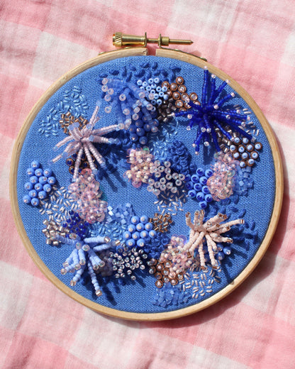 Embroidery hoop with blue floral design on a pink checkered background
