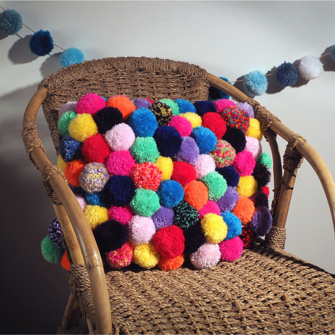 Wicker chair with a colorful pom-pom Cushion against a neutral background