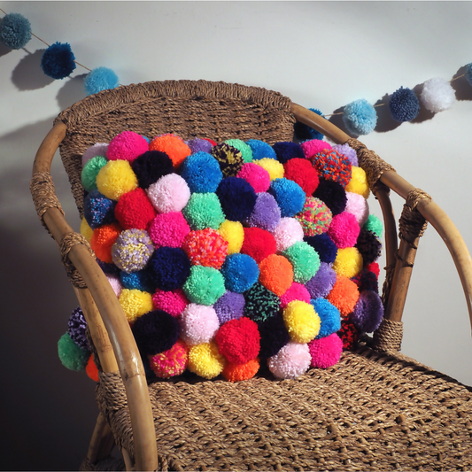 Wicker chair with a colorful pom-pom Cushion against a neutral background