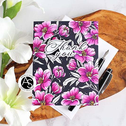 Floral notebook with 'Thank you' text on a wooden surface with flowers and pens.