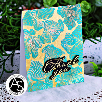 Card with teal floral pattern and 'Thank you' text on a decorative surface with plants in the background