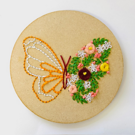Embroidery hoop with a butterfly and floral design on beige fabric.