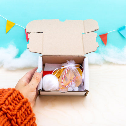 Hand holding a box with festive items against a light blue background with colorful flags.