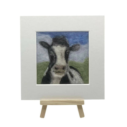 Felted artwork of a cow on a small easel with a white background