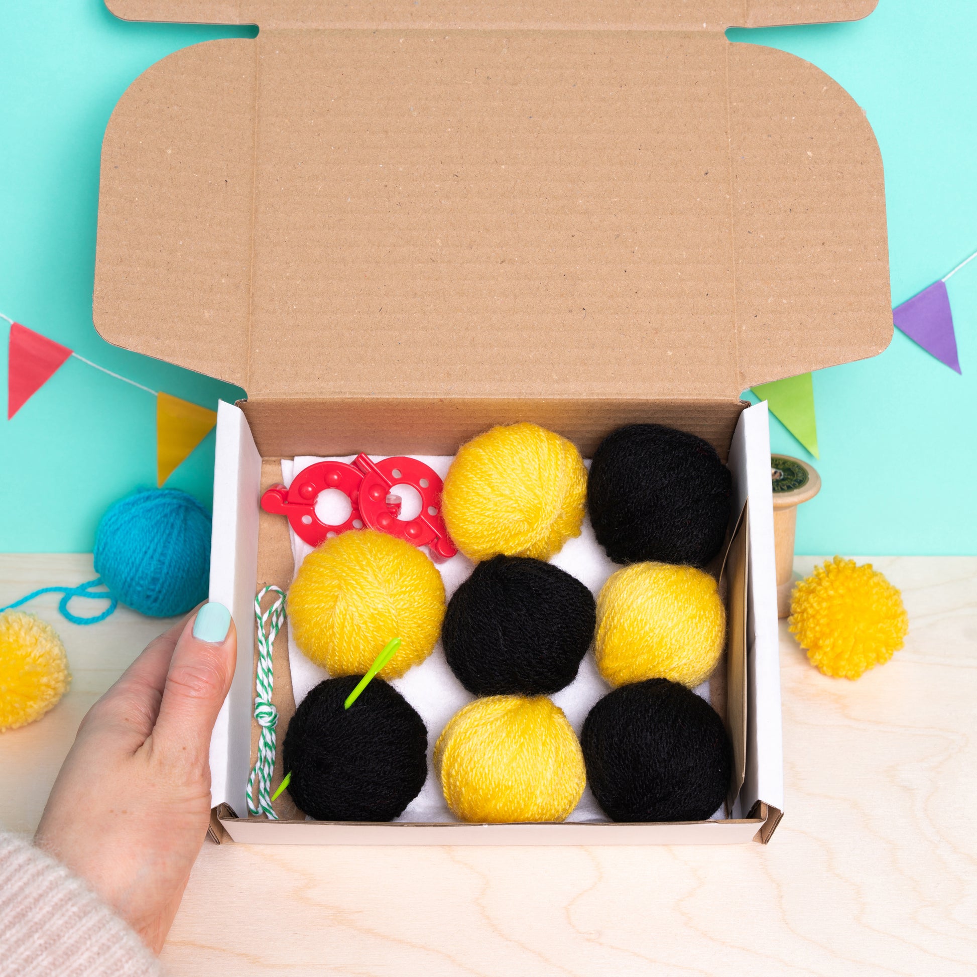 Box of black and yellow pom-poms with a hand holding it against a colorful background