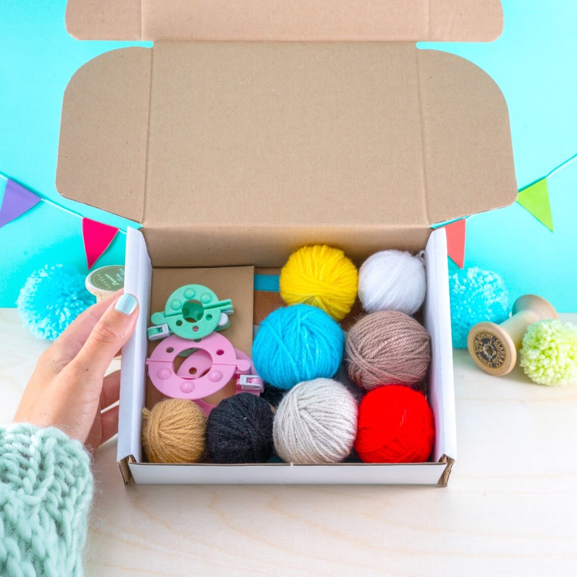Box of colorful yarn balls and crafting tools on a light blue background