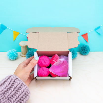 Hand holding a box of pink yarn against a blue background with decorative flags.