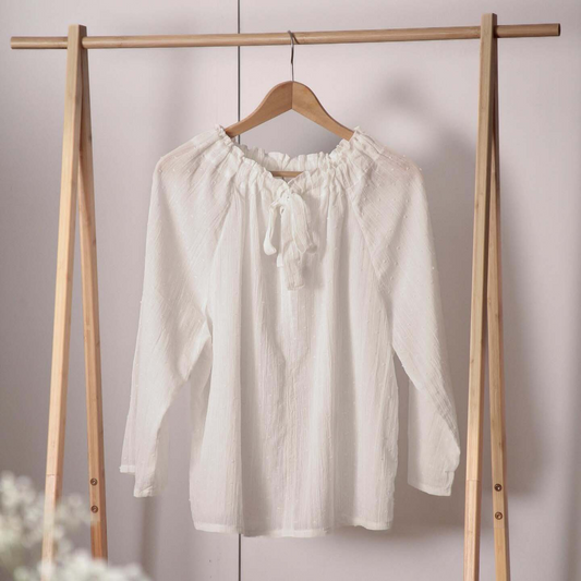 White blouse on a wooden hanger against a plain background