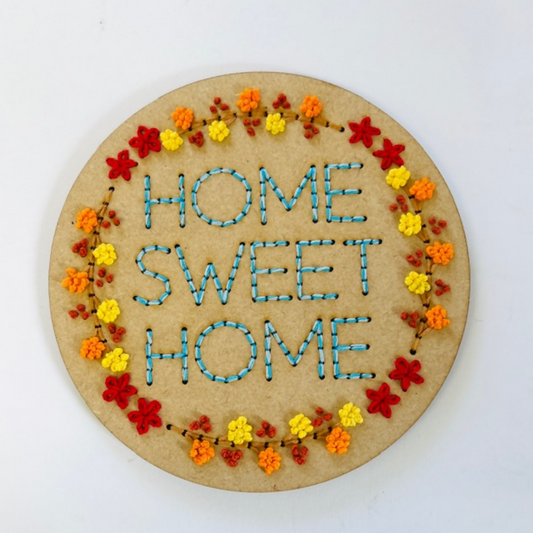 Round embroidered sign with 'Home Sweet Home' text and floral border on a white background