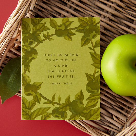 Green card with leaf pattern and motivational quote on a woven surface with a green apple.