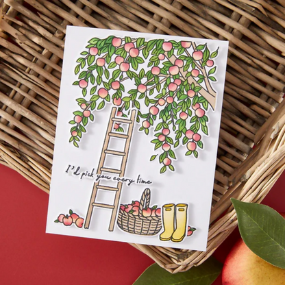Card with a ladder, basket of apples, and boots on a woven surface with a red background.