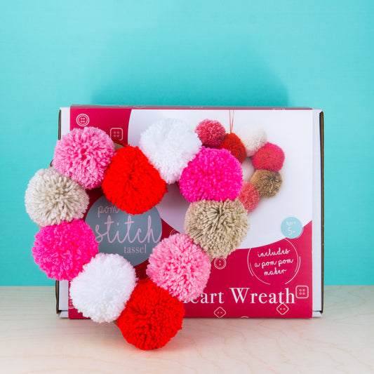 Pom-pom heart wreath craft kit with colorful pom-poms on a teal background
