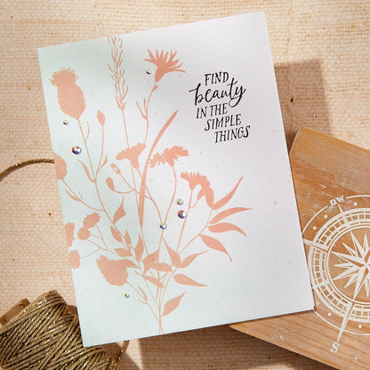 Card with floral design and 'Find beauty in the simple things' text on a wooden surface.