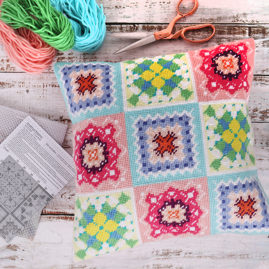 Colorful crocheted cushion with square patterns on a wooden surface with yarn and scissors.
