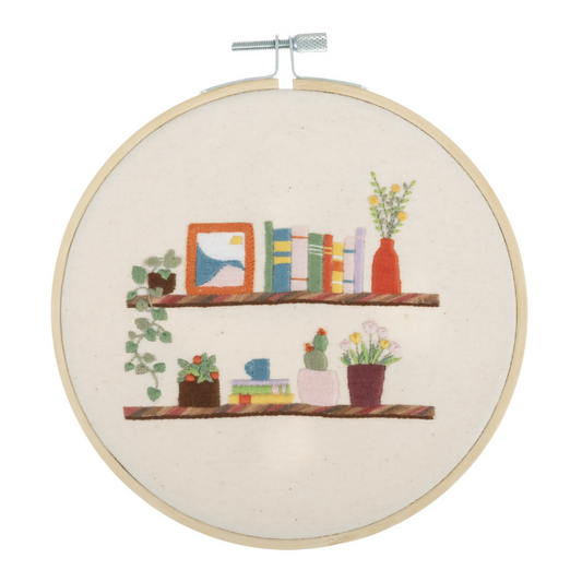 Embroidery hoop with a colorful depiction of books and plants on shelves.